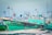 A green and black boat is docked at a busy harbor. The boat is accompanied by several other vessels, and there are Indian flags flying from some masts. The scene captures a vibrant marine setting with ropes, nets, and equipment scattered around the dock.