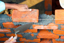 Close-up of skilled hands laying bricks on a sunny construction site.