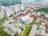 An aerial view of a large urban complex featuring multiple modern buildings with red and white facades surrounded by greenery. The layout includes several rectangular structures with flat roofs, wide courtyards, and open spaces. In the distance, there are taller residential buildings with consistent architectural styles.