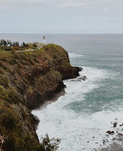 A rugged coastline with crashing waves and a lone lighthouse under a cloudy Pacific Northwest sky.