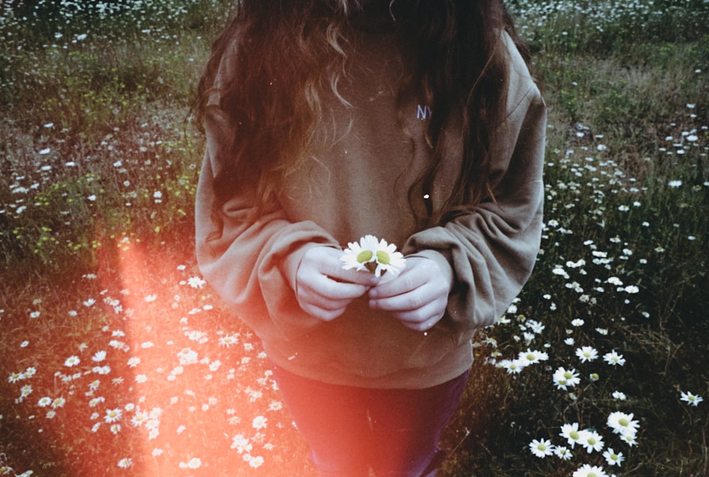 a girl standing in a field with a flower in her hands