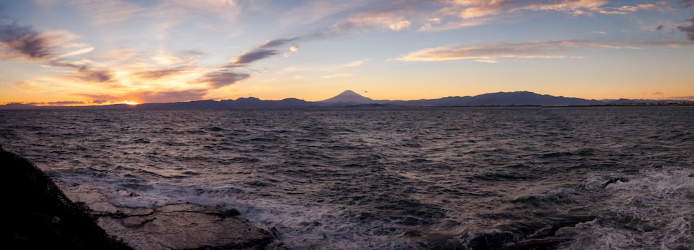 the sun is setting over the ocean with mountains in the distance