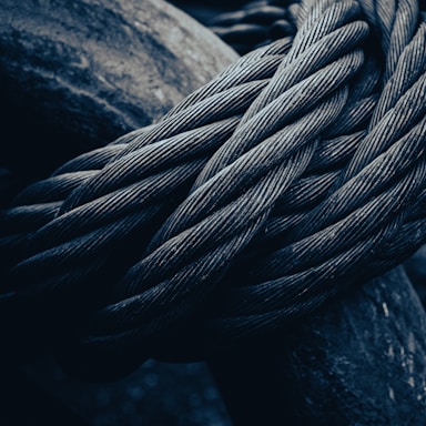 Thick, intertwined metal cables are closely packed, exhibiting their intricate texture. The image focuses on the rugged and durable nature of the steel wires, highlighting their complex weave and robust appearance under low lighting conditions.