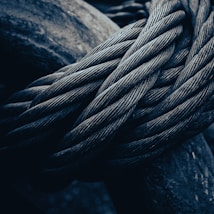 Thick, intertwined metal cables are closely packed, exhibiting their intricate texture. The image focuses on the rugged and durable nature of the steel wires, highlighting their complex weave and robust appearance under low lighting conditions.