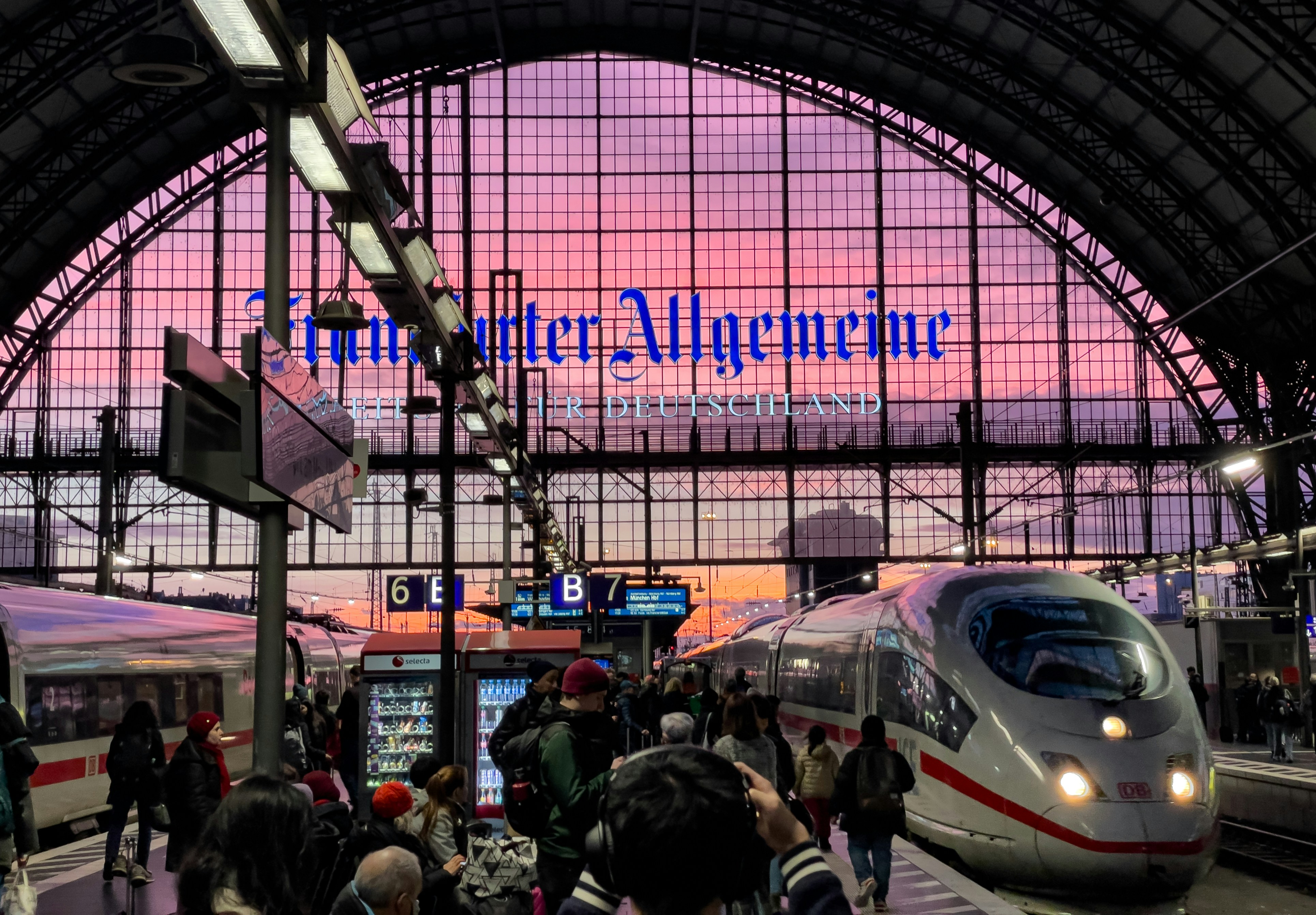 a group of people standing next to a train at a train station, A vibrant scene at Frankfurt Main Train Station with the evening sky visible through the vast glass roof. Commuters and travelers are near a parked ICE train, with "Frankfurter Allgemeine" advertisement prominent above.