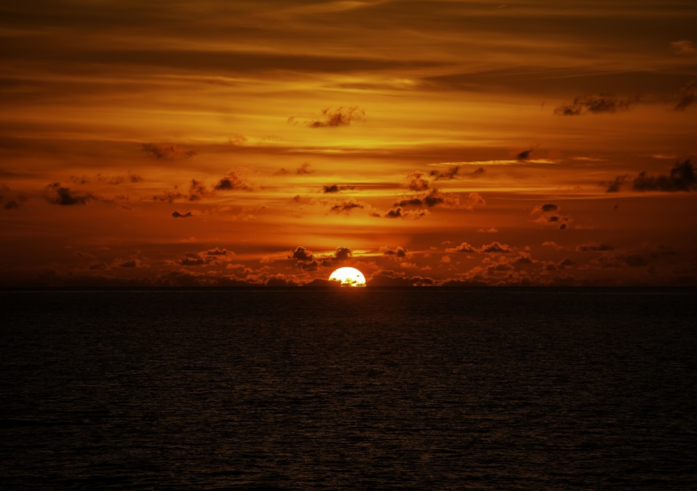 the sun is setting over the ocean on a cloudy day