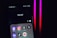 A smartphone screen displays a folder labeled 'Social,' containing icons for various social media apps, including Facebook, Instagram, Threads, X, LinkedIn, TikTok, and YouTube. The background is dark with pink and red neon lights.