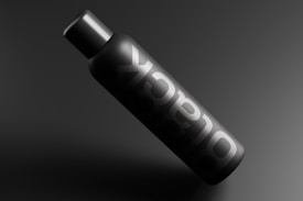 A sleek, matte black bottle with the word 'black' prominently displayed in white, lying diagonally against a dark background. The design conveys a minimalist and modern aesthetic.