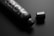 A sleek, black matte bottle lies on a dark surface with the cap placed next to it. The bottle features bold silver text with a minimalist design, creating a sophisticated and modern look.