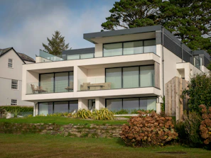 A modern villa with large glass windows surrounded by lush greenery under a clear blue sky