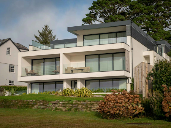 A modern villa with large glass windows surrounded by lush greenery under a clear blue sky.