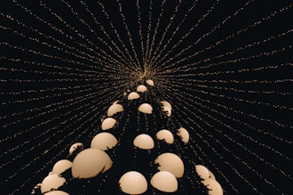 A captivating perspective of a conical shape made up of several glowing spherical orbs, creating a visually striking effect. The structure is framed against a dark background filled with lines of small, glowing dots converging from the edges to the top, offering a sense of depth and infinity.