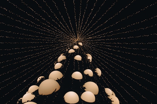 A captivating perspective of a conical shape made up of several glowing spherical orbs, creating a visually striking effect. The structure is framed against a dark background filled with lines of small, glowing dots converging from the edges to the top, offering a sense of depth and infinity.