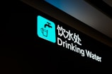 A sign for drinking water with a blue icon featuring a faucet above a glass. The text is written in both Chinese and English, illuminated against a black background.