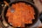 A large frying pan filled with evenly arranged rectangular tofu pieces, coated with a reddish sauce and sprinkled with sesame seeds. A metal spatula with a wooden handle is resting against a few pieces of tofu on the left side of the pan.