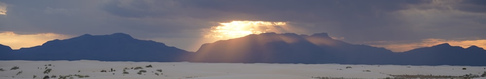 the sun is shining through the clouds over the mountains