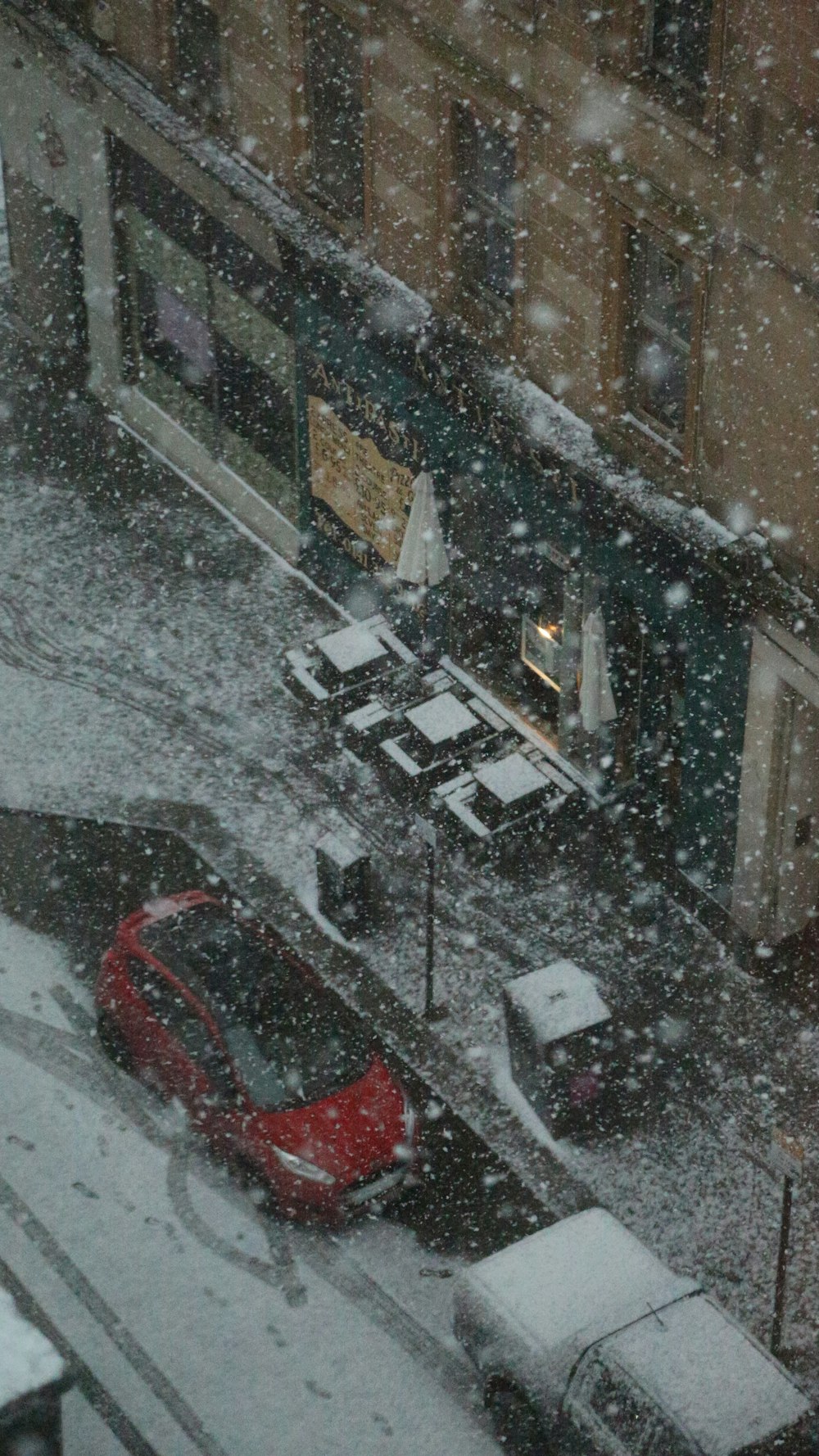 a red car driving down a snow covered street