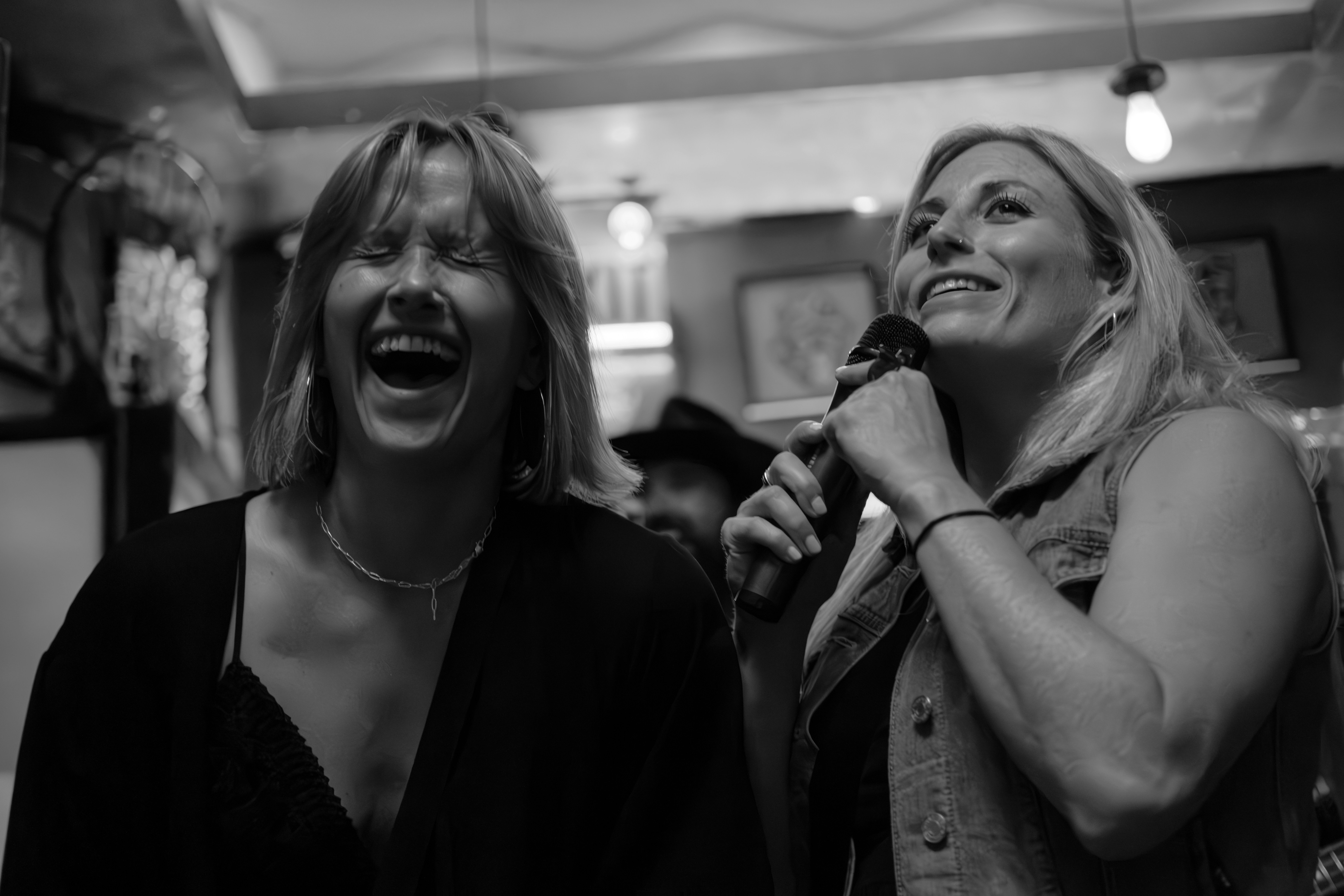 Dwie kobiety śpiewają i śmieją się razem podczas występu karaoke.