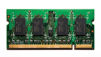 A compact green circuit board features multiple black rectangular chips surrounded by intricate gold pathways and connectors. The detailed design is typical of a RAM module used in computers.
