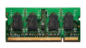 A compact green circuit board features multiple black rectangular chips surrounded by intricate gold pathways and connectors. The detailed design is typical of a RAM module used in computers.