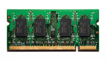 A compact green circuit board features multiple black rectangular chips surrounded by intricate gold pathways and connectors. The detailed design is typical of a RAM module used in computers.