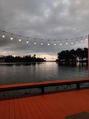 Warm evening view of a wooden deck with soft lighting beside a flowing river embraced by lush forest.