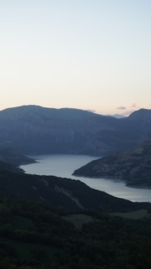 A serene landscape featuring gentle hills and a calm lake under a twilight sky.