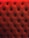 A close-up of a tufted, padded surface with a luxurious texture. The material is upholstered in a deep red color, and small buttons create a diamond pattern.