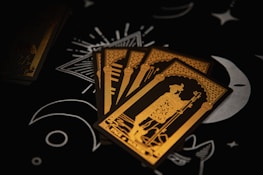 Four tarot cards are spread out on a dark surface, featuring intricate gold line art of a robed figure holding a staff. The background includes black with white moon and star illustrations, adding a mystical ambiance.