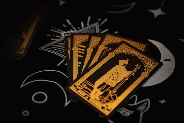 Four tarot cards are spread out on a dark surface, featuring intricate gold line art of a robed figure holding a staff. The background includes black with white moon and star illustrations, adding a mystical ambiance.