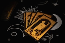Four tarot cards are spread out on a dark surface, featuring intricate gold line art of a robed figure holding a staff. The background includes black with white moon and star illustrations, adding a mystical ambiance.