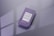 A purple business card with a vertical white text design. The card features one rounded corner and is placed on a reflective, smooth surface. Soft shadows create a subtle depth effect, while a blurred window pattern is faintly visible in the background.