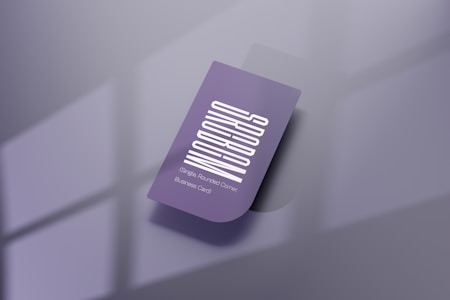 A purple business card with a vertical white text design. The card features one rounded corner and is placed on a reflective, smooth surface. Soft shadows create a subtle depth effect, while a blurred window pattern is faintly visible in the background.