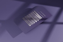 A business card with bold, stylized text reading 'SPREAD' is prominently displayed. The card is in a folded position, casting a soft shadow over a smooth, purple surface. The lighting creates a modern and professional ambiance, with a subtle gradient in the background.