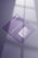 Two purple business cards are placed on a reflective surface. One card is facing up showing a stylized white text and the other is facing down displaying a QR code and details in white. The lighting creates soft shadows and a subtle window reflection on the surface.