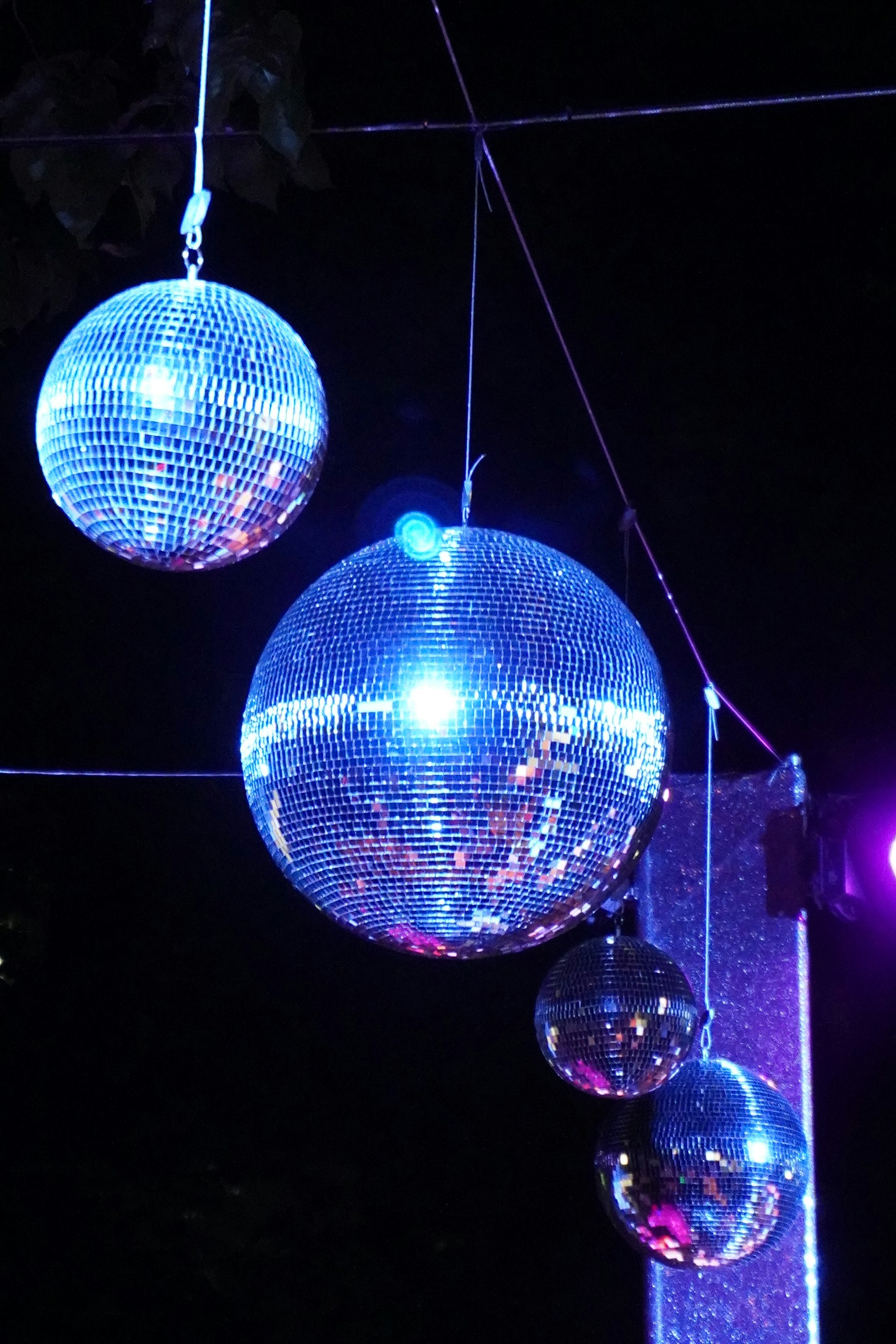 Three mirror disco balls are hanging against a dark background. Blue and purple lights reflect off the mirrored surfaces, creating a vibrant and festive shimmer.