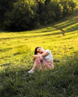 A woman sitting peacefully on a soft blanket outdoors, surrounded by gentle greenery.