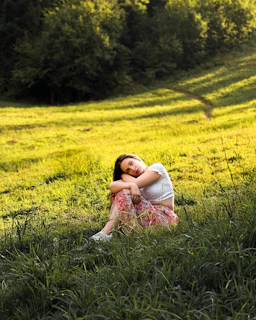 A serene woman sitting peacefully in nature, bathed in soft morning light.