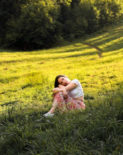 A thoughtful woman meditating outdoors surrounded by soft greenery and warm sunlight.