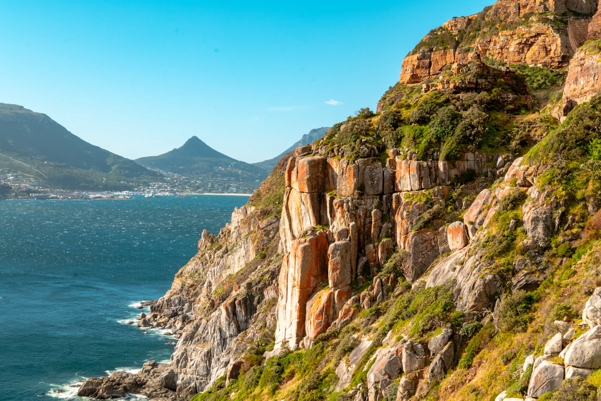 Orange sandstone cliffs above the sea on Chapman's Peak, with a bay and peaks behind