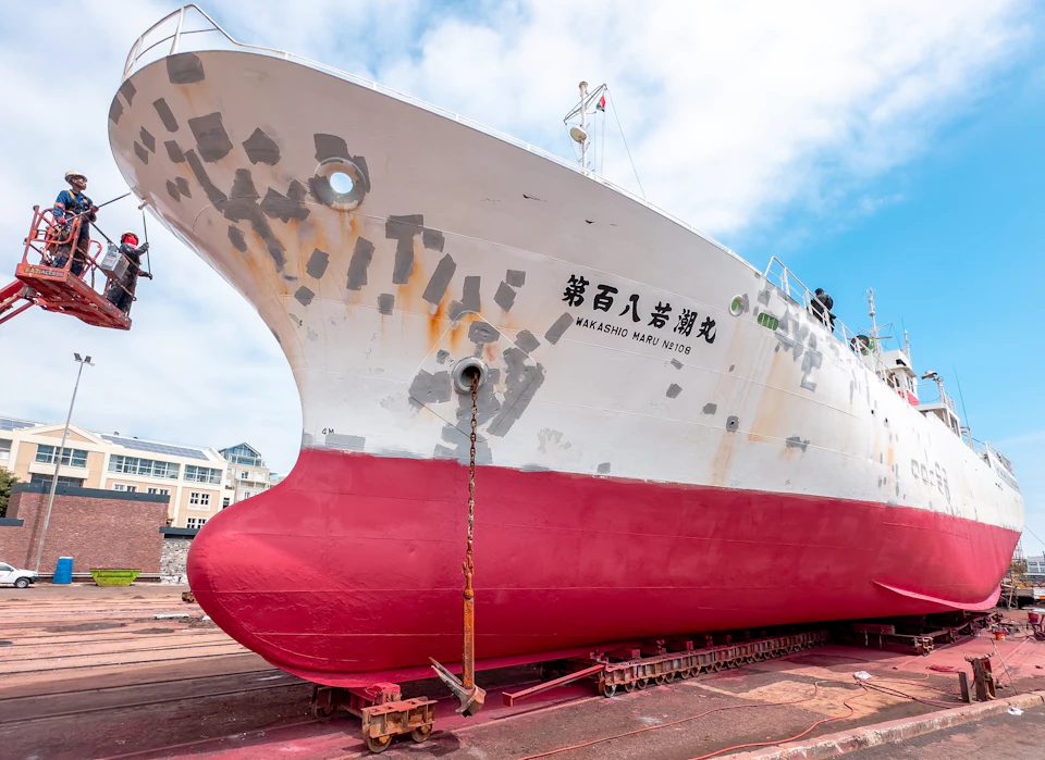 Workers on a lift treating the hull of a ship on a slipway