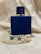 Elegant deep blue perfume bottle resting on a reflective surface with subtle golden highlights.