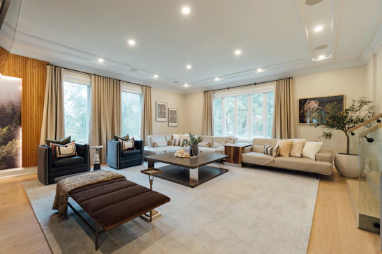 A luxurious living room featuring soft beige walls, gold accents, and sleek black furnishings bathed in warm natural light.