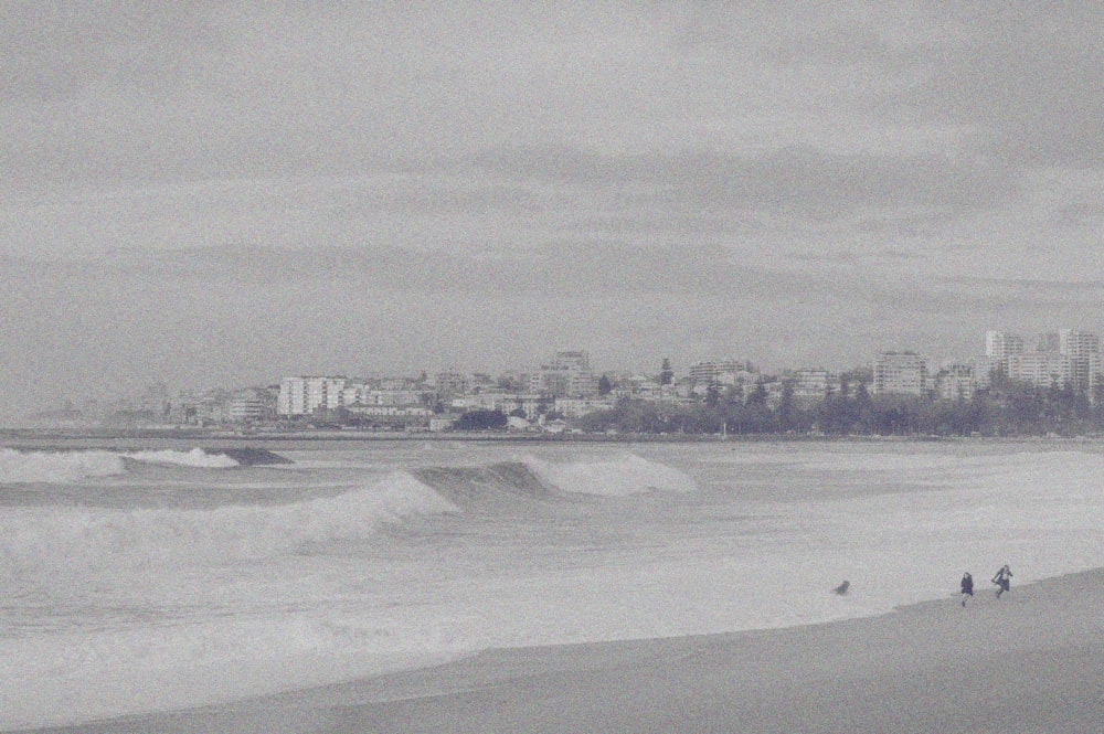 a black and white photo of people walking on the beach