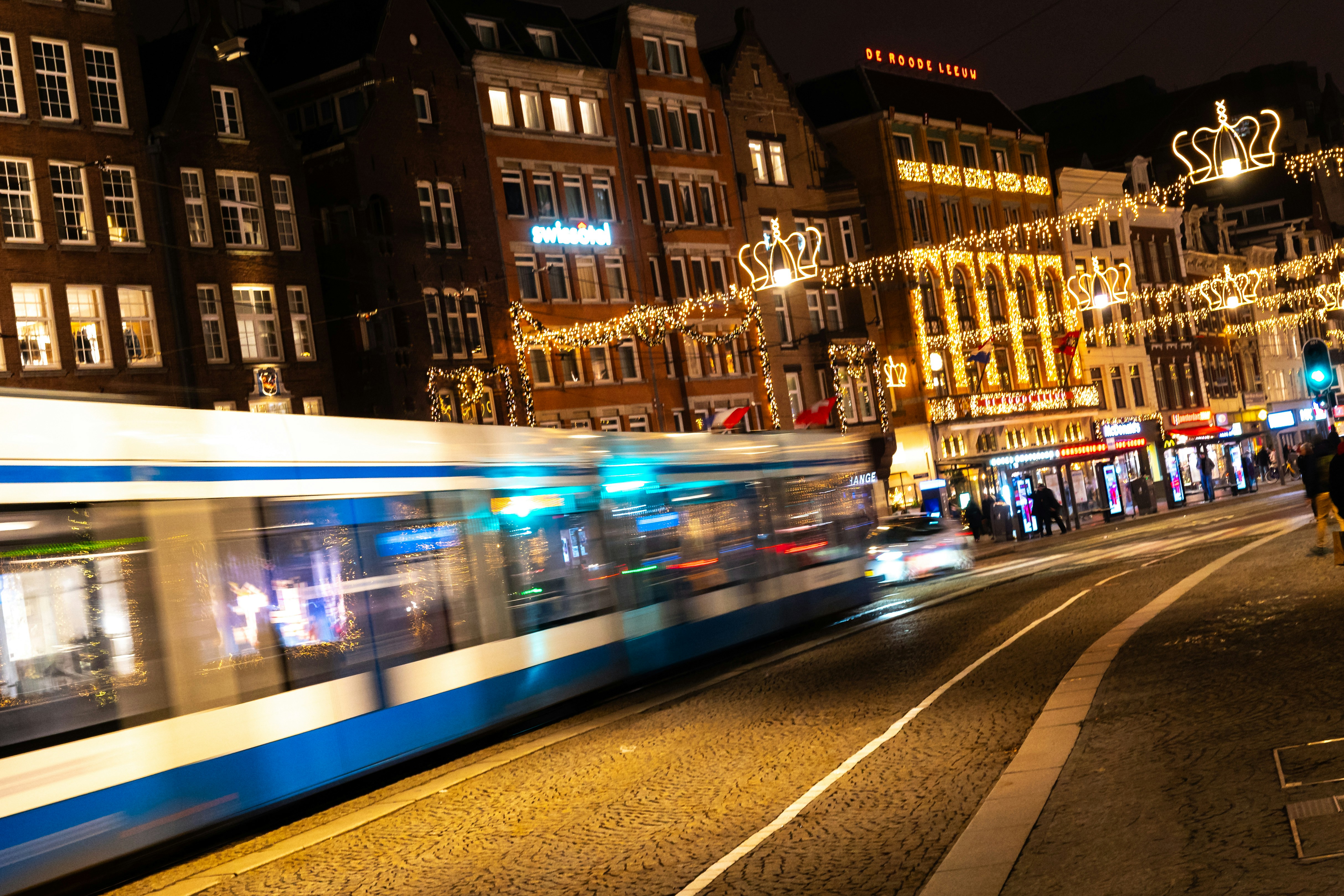 a blue and white train traveling down a street next to tall buildings in Amsterdam