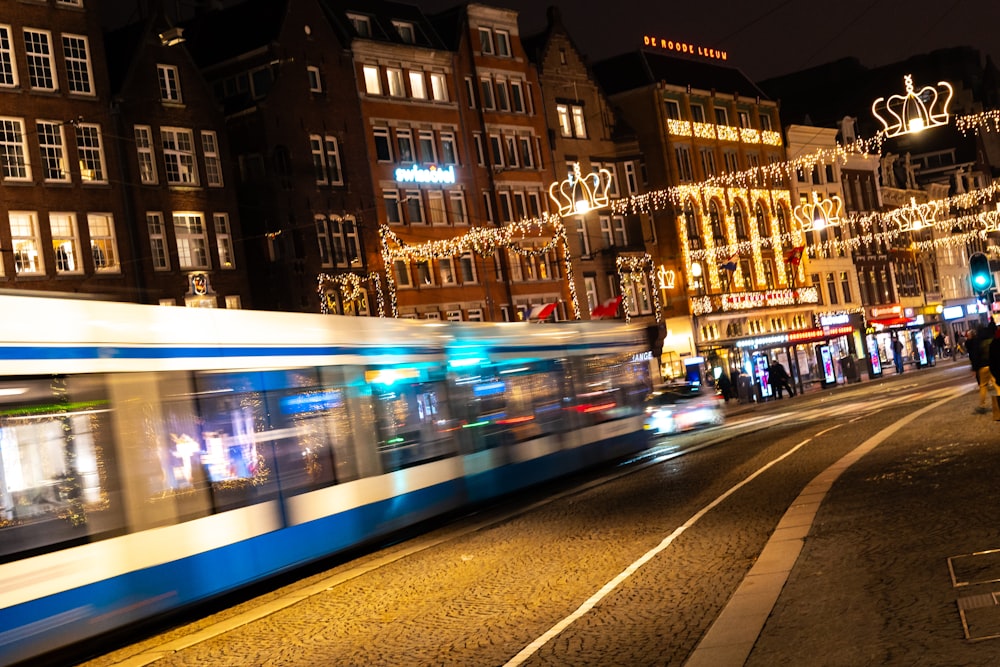 a blue and white train traveling down a street next to tall buildings