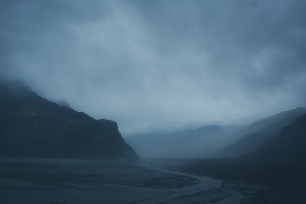 a river running through a valley under a cloudy sky