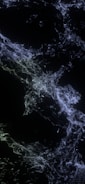 Suspended, interconnected strands of blue and white particles create an abstract, web-like pattern against a dark background, resembling cosmic or neural structures.
