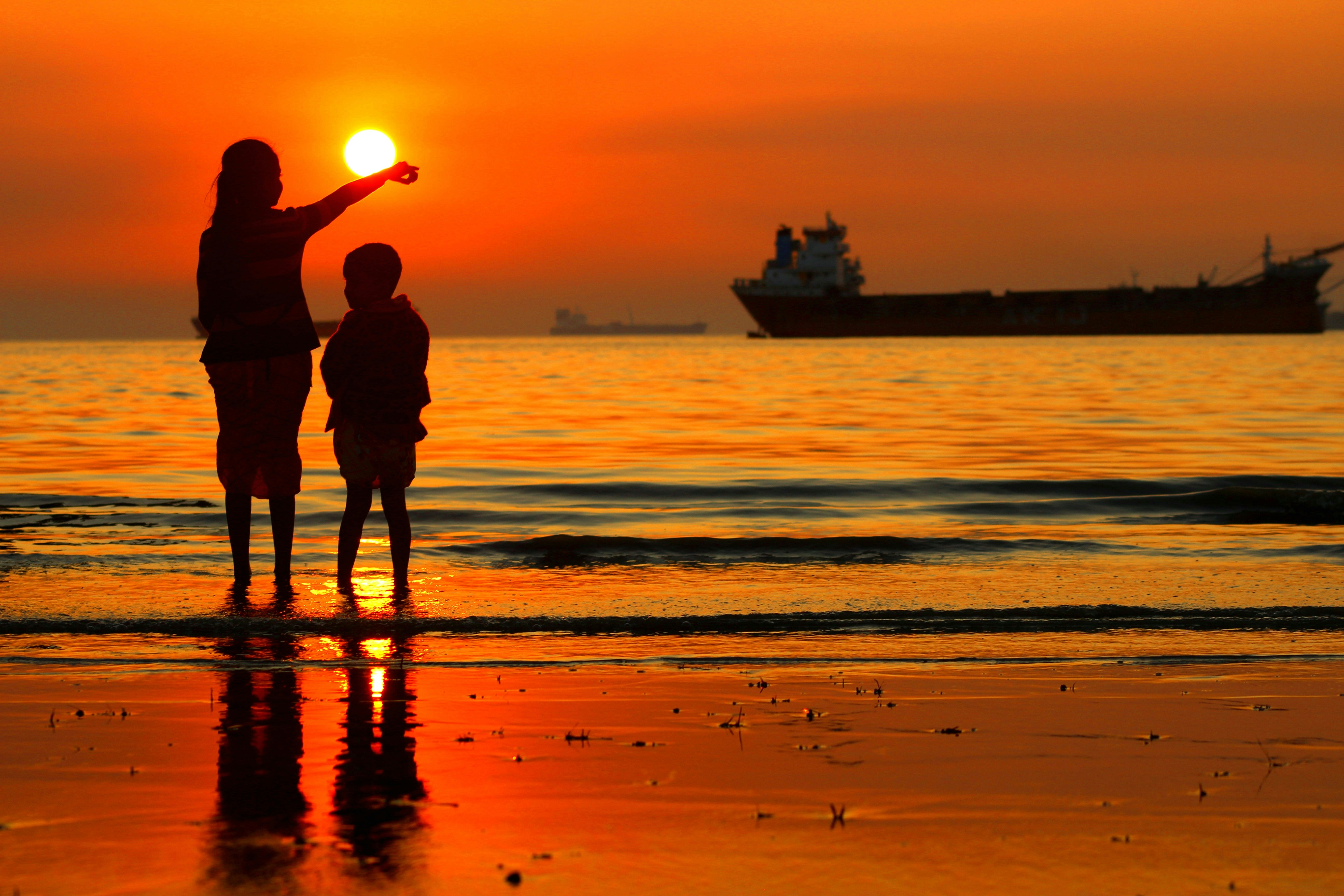 seorang wanita dan seorang anak berdiri di pantai saat matahari terbenam