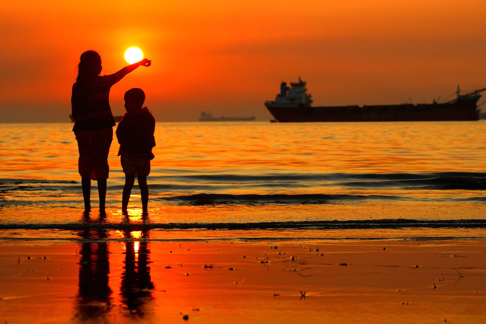 a woman and a child standing on a beach at sunset